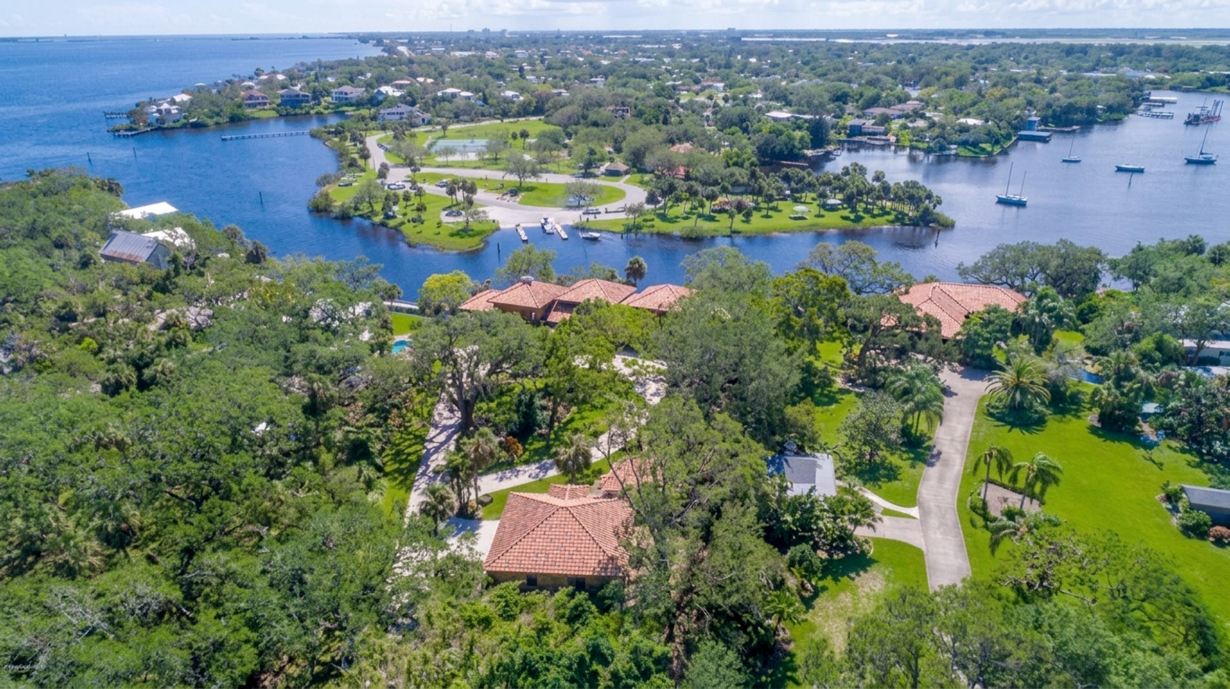 Wide pulled-back aerial showing full grounds, tree canopy, and property boundary against the water and neighboring estates.