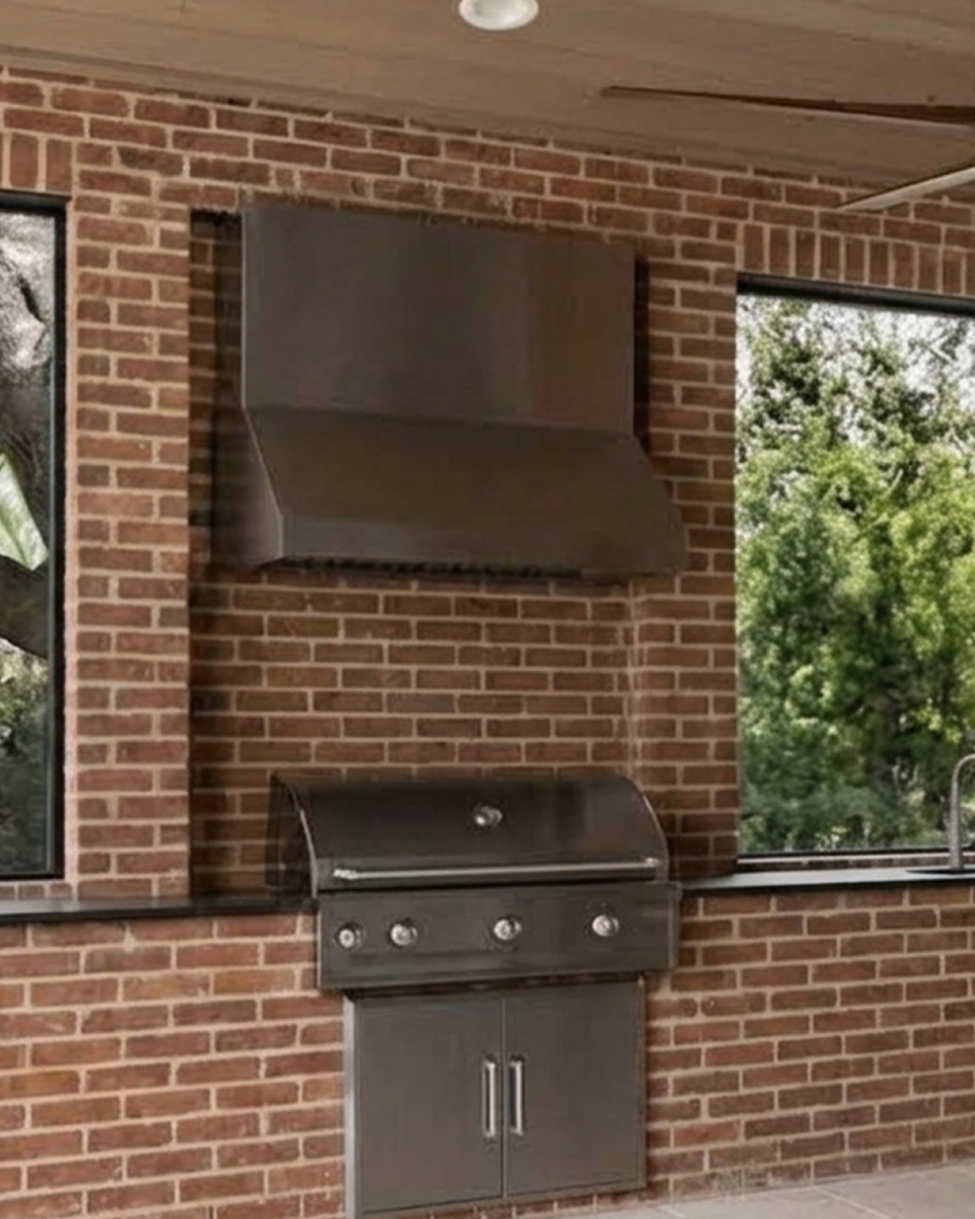 Outdoor brick lanai kitchen, hood and grill centered between two windows.